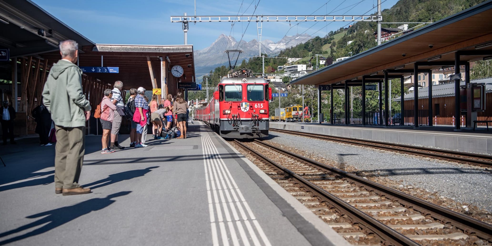 Rhb fährt in Bahnhof rein, Passagiere warten auf der Linken Seite auf dem Perron