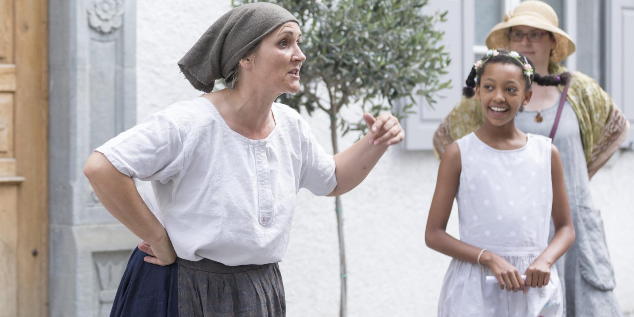 Szene aus Theaterstück, Frau mit Kopftuch und historischer Bauernkleidung daneben zwei weitere Personen welche sie anschauen