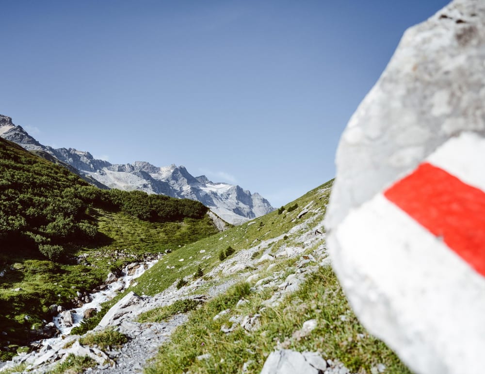 Sommer Kennzeichnung Wanderweg an Stein auf der rechten Seite, im Hintergrund Bergpanorama