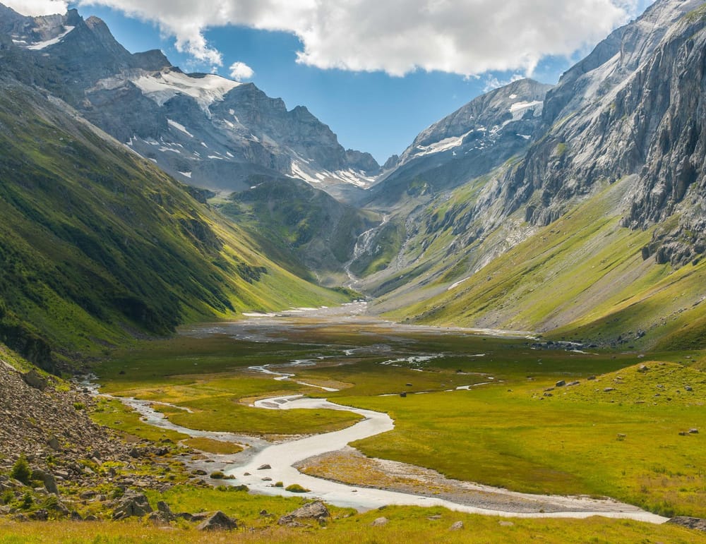 Vogelperspektive grüne Wiesen umrahmt von Bergen und ein Flussbett in der Mitte