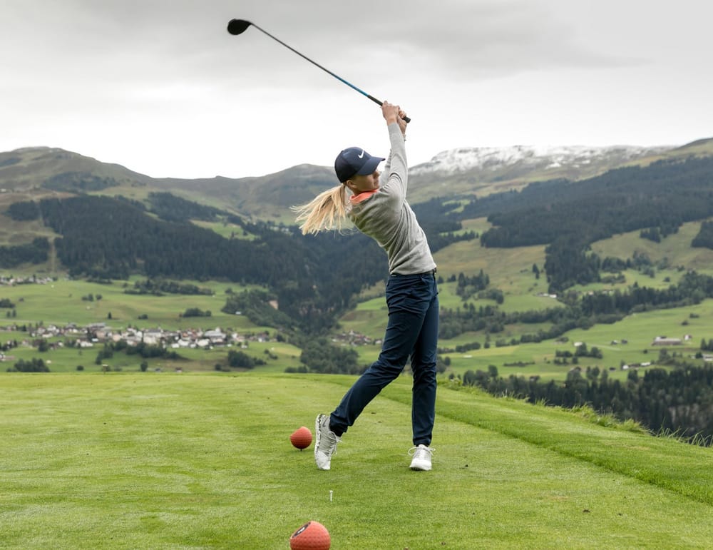 Frau beim Abschlag auf Golfplatz in der Surselva