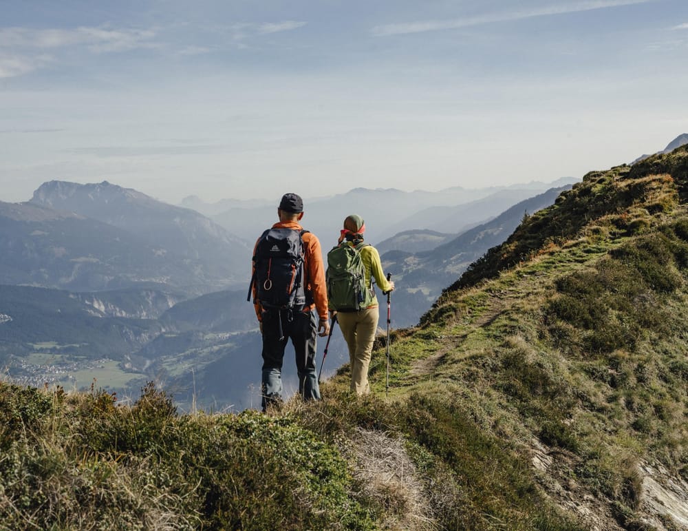 Zwei Personen wandern auf einem Grad auf der linken Seite Bergkulisse