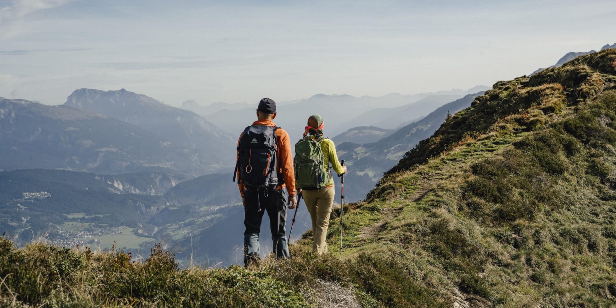 Zwei Personen wandern auf einem Grad auf der linken Seite Bergkulisse