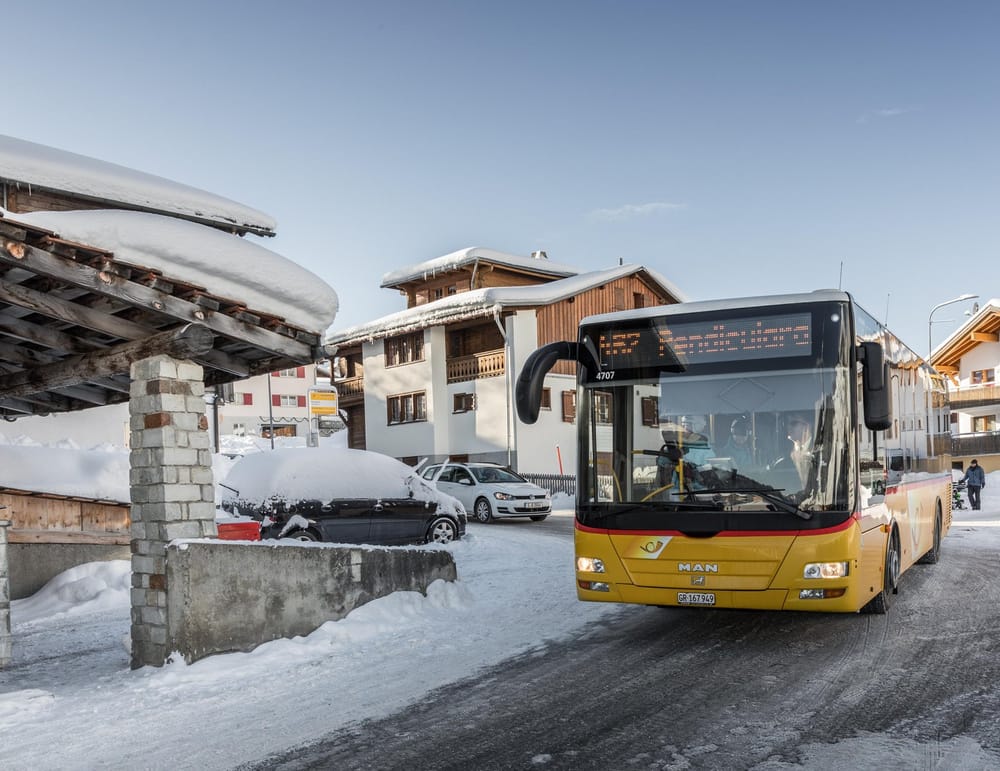 Postauto fährt im Winter Haltestelle in einem Dorf an