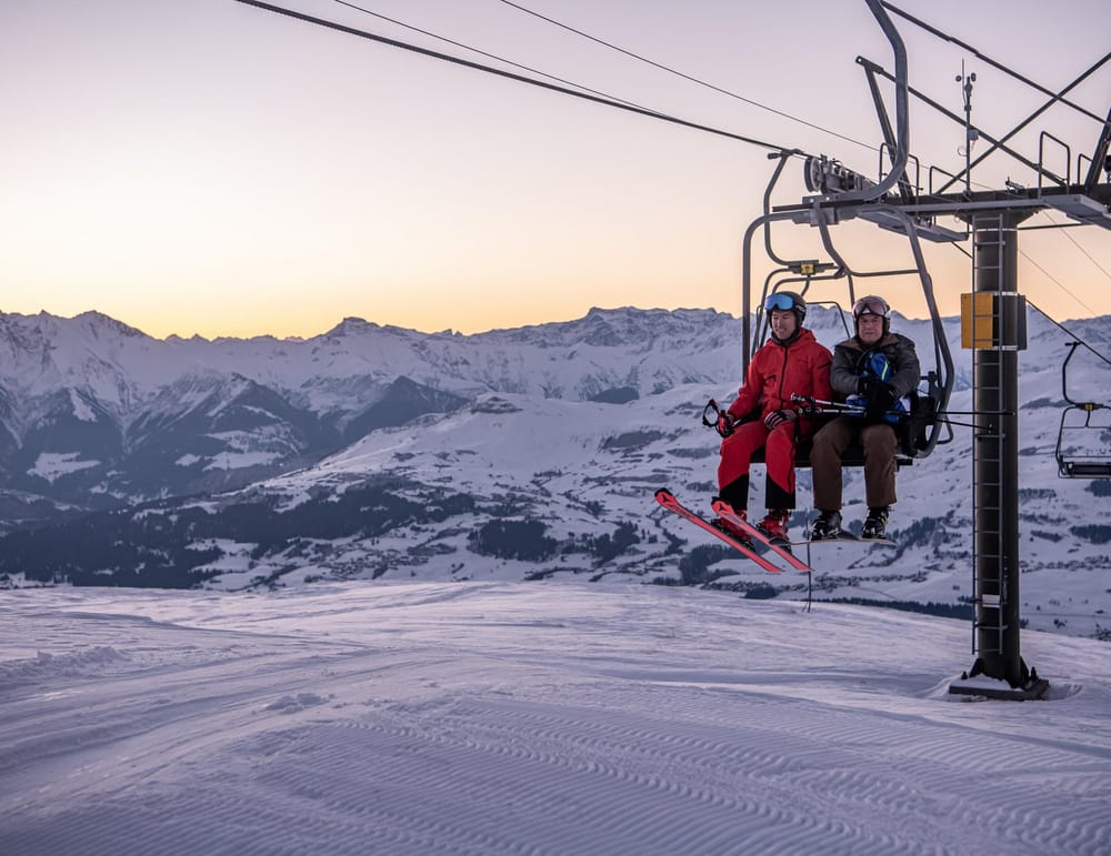 Sessellift mit zwei Skifahrer darauf in der Abenddämmerung